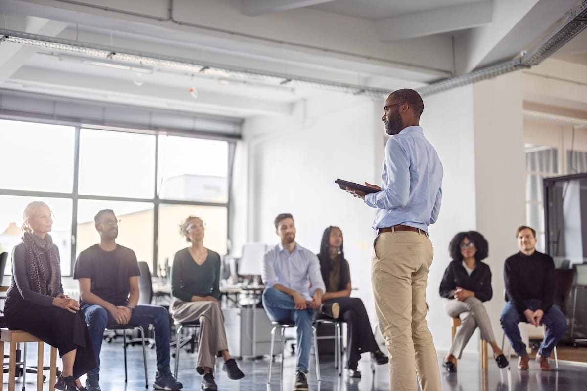 a man speaking in front of a group of people sitting in chairs