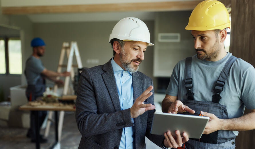 Male interior designer and manual worker communicating while working on digital tablet during home renovation process.