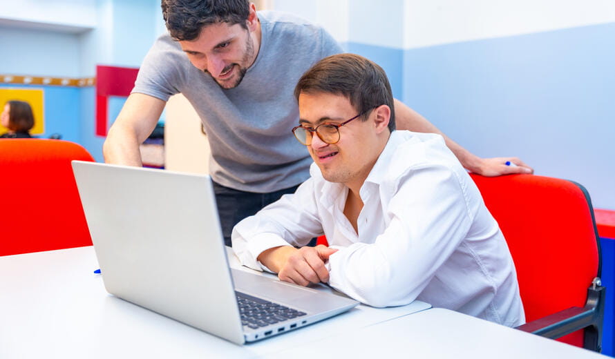 Friendly adult male teacher helping a man with down syndrome during computing class