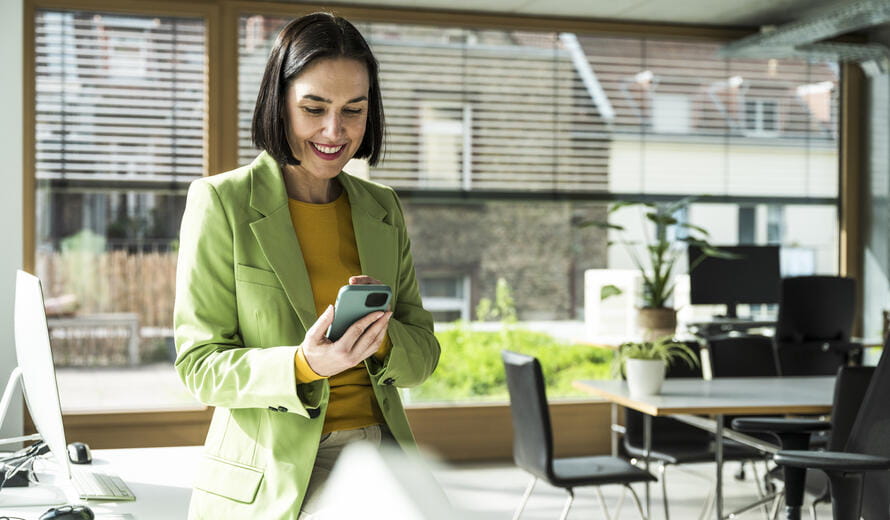 Happy mature businesswoman using smart phone sitting on desk in office