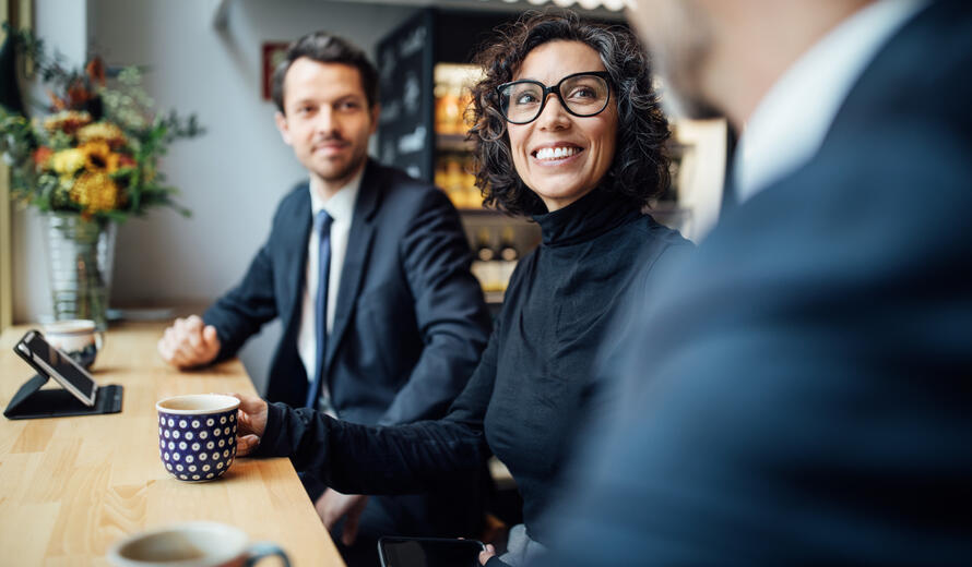 A group of three business people, including a mature woman, sitting at a coffee shop and having a discussion. Perfect for resource hub imagery.