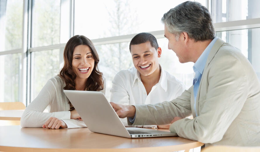 Mature financial consultant advising a happy young couple while using a laptop. Horizontal shot.