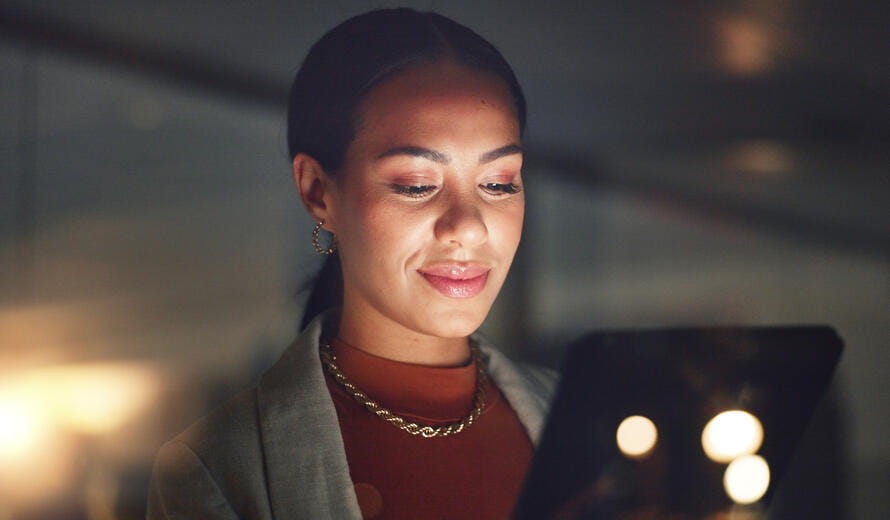 A happy corporate employee working late, using a tablet to search online reports and plan websites, highlighting digital data and social network app usage.