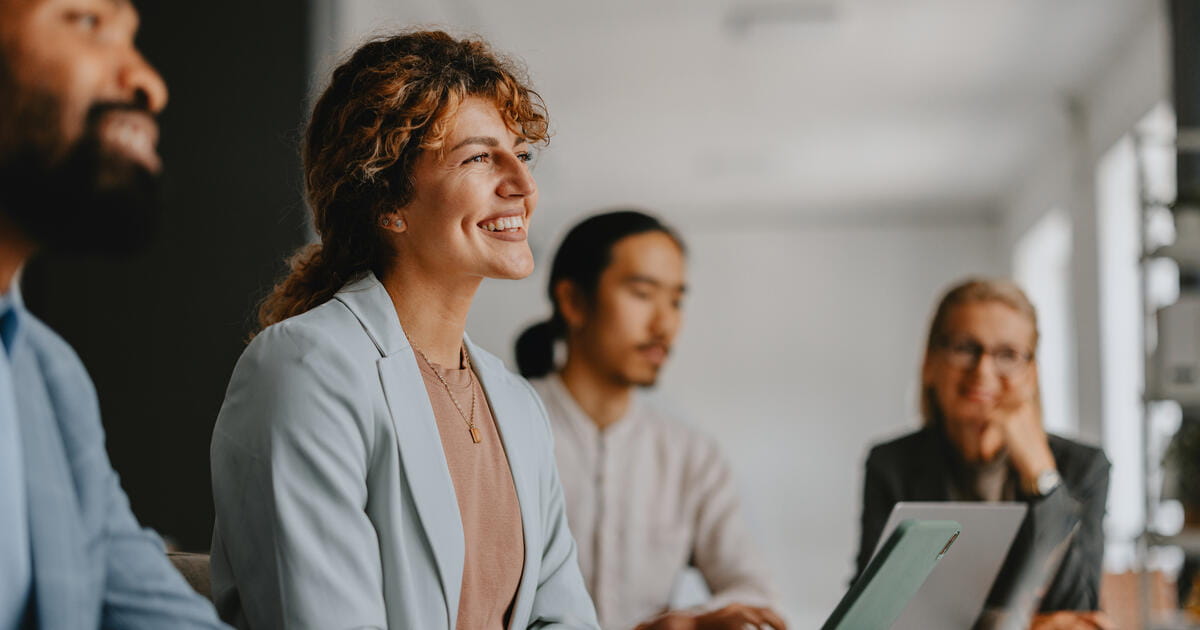 A diverse group of business professionals engaged in a collaborative meeting at a modern office. They are working together, sharing ideas, and using laptops.