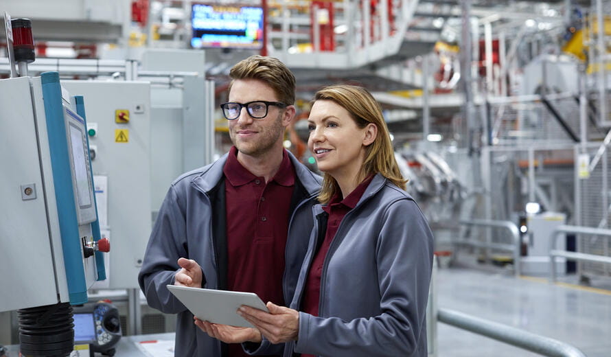 Smiling engineers using tablet PC by control panel. Confident workers are wearing uniform at automobile industry. Male and female professionals are working at car plant.